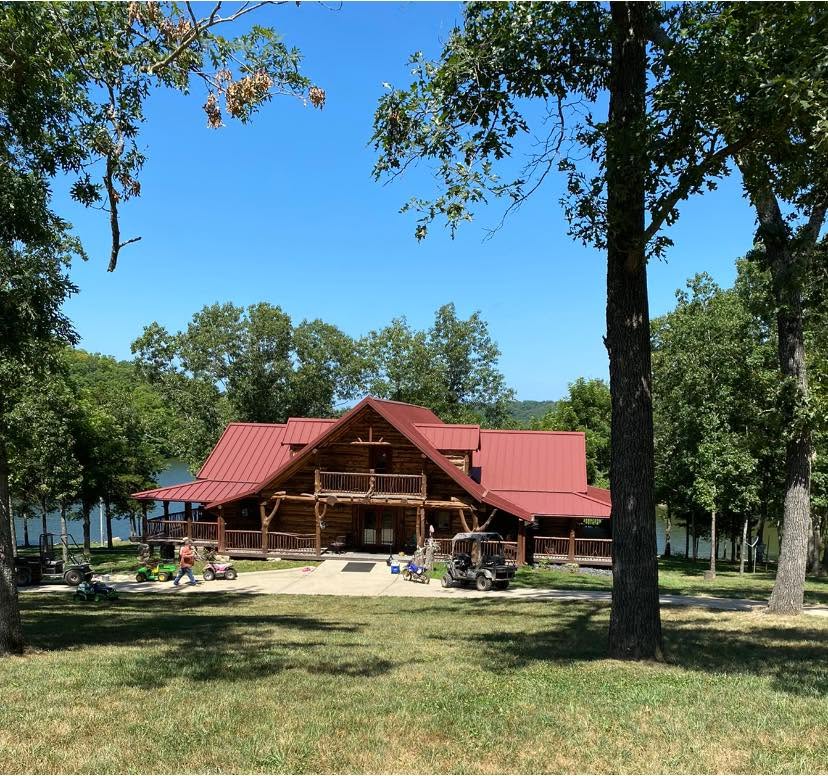 Large cedar log lodge with red metal roof among trees