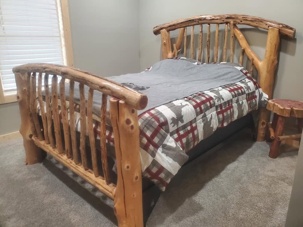 Handcrafted cedar log queen bed with plaid bedding in a finished cabin bedroom
